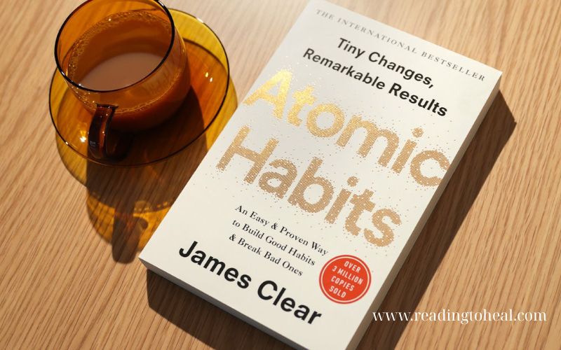 Atomic Habits book by James Clear on a wooden table next to a cup of tea