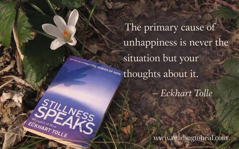 Stillness Speaks book on forest floor with white flower and Eckhart Tolle quote about thoughts and unhappiness